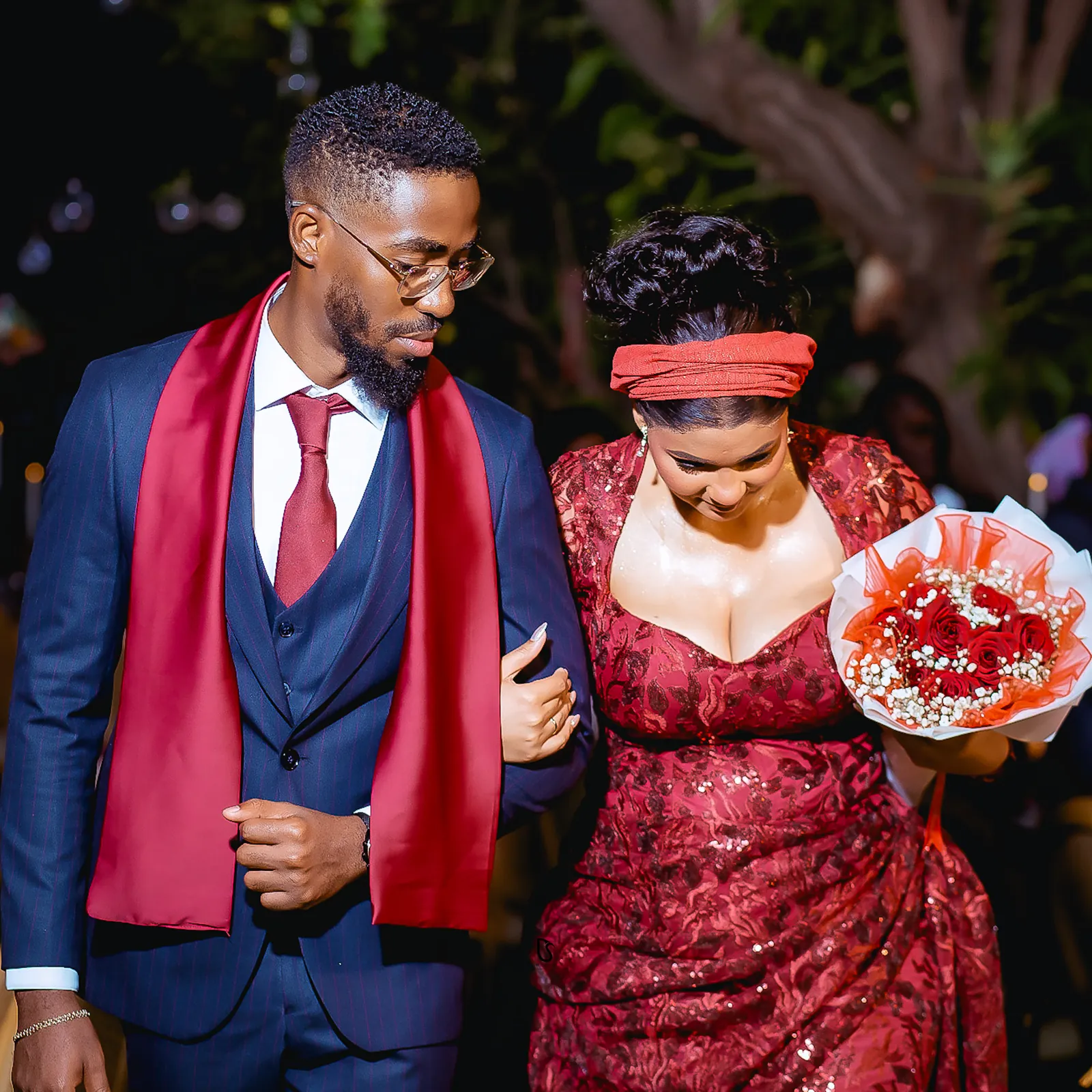 Noivos de vermelho e azul-marinho de braço dado, a noiva com bouquet de rosas